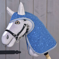 Pláštěnka Dolly (softshell) od Hobby Horse LarDen se šedým Hobby Horse s modrou přikrývkou se vzorem kapek vody a uzdečkou na dřevěné tyči – perfektní pro hru za každého počasí na pozadí rustikálních dřevěných prken.
