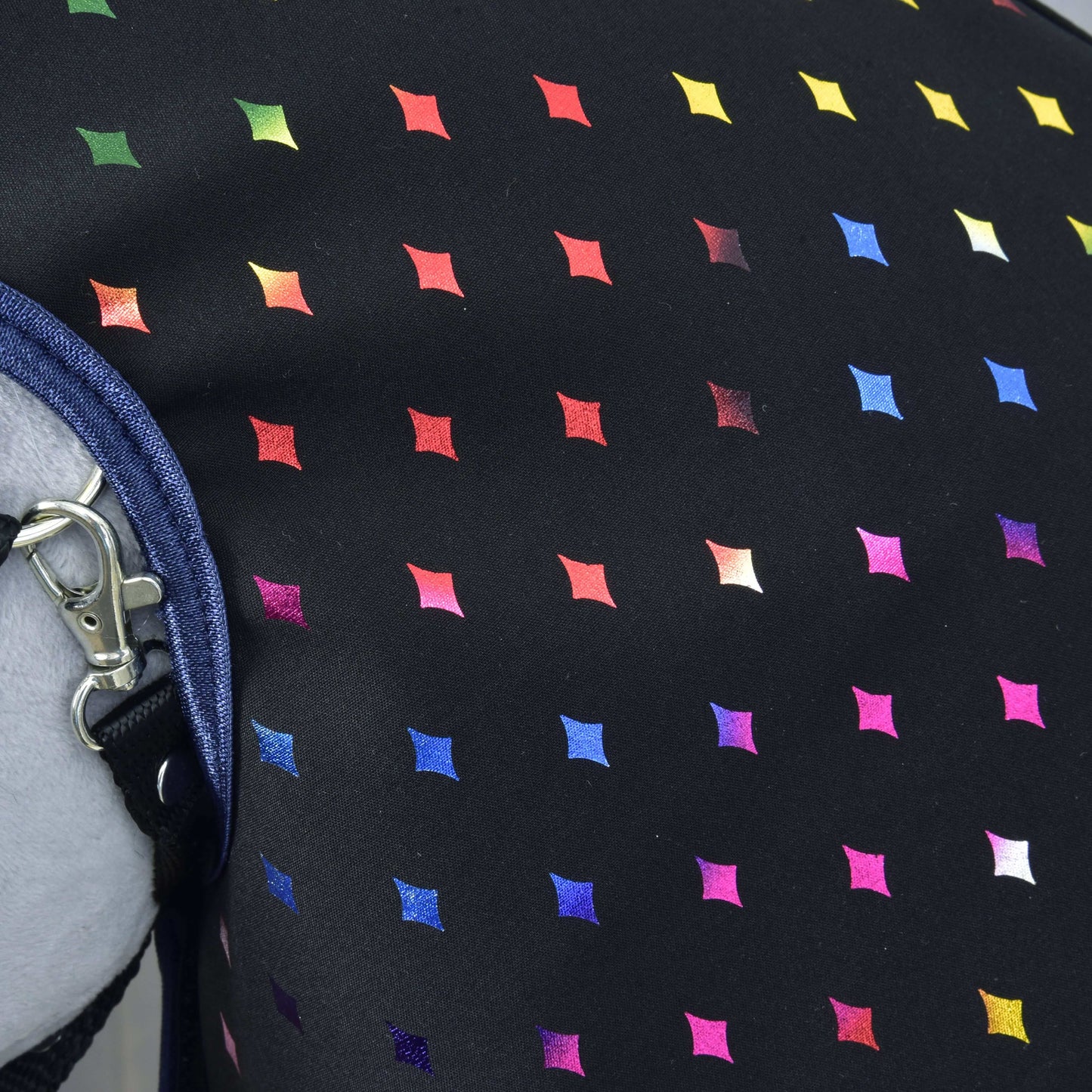 Detail Pláštěnky Sparkling Queen od Hobby Horse LarDen s černou látkou s mřížkou z malých barevných kosočtverců. Kovová spona a modrý džínový pásek vlevo zdůrazňují její využití za každého počasí.