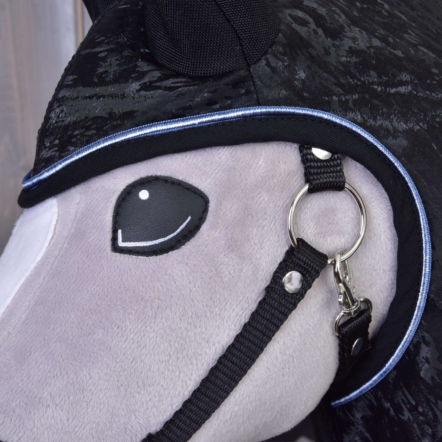 Detail obličeje plyšového Hobby Horse s černou uzdečkou, černou kapucí s modrým lemováním a světle šedým čenichem. Kombinujte tohoto roztomilého Hobby Horse LarDen s Raincoat Silver Stone nebo dalšími zábavnými doplňky pro Hobby Horse.