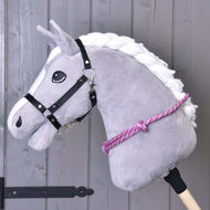 Nákrčník s růžovým proužkem od Hobby Horse LarDen na šedé plyšové koňské hlavě s bílou hřívou, černou uzdečkou a růžovo-bílým nákrčníkem na dřevěné tyči, ideální pro nácvik jízdy bez uzdečky před šedou dřevěnou stěnou.