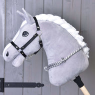 Nákrčník se stříbrným proužkem od Hobby Horse LarDen na plyšovém šedém Hobby Horse s bílou hřívou, černou uzdečkou a ručně vyráběným šedo-bílým cordeem, zobrazený před dřevěnými prkny s černým kovovým kováním.