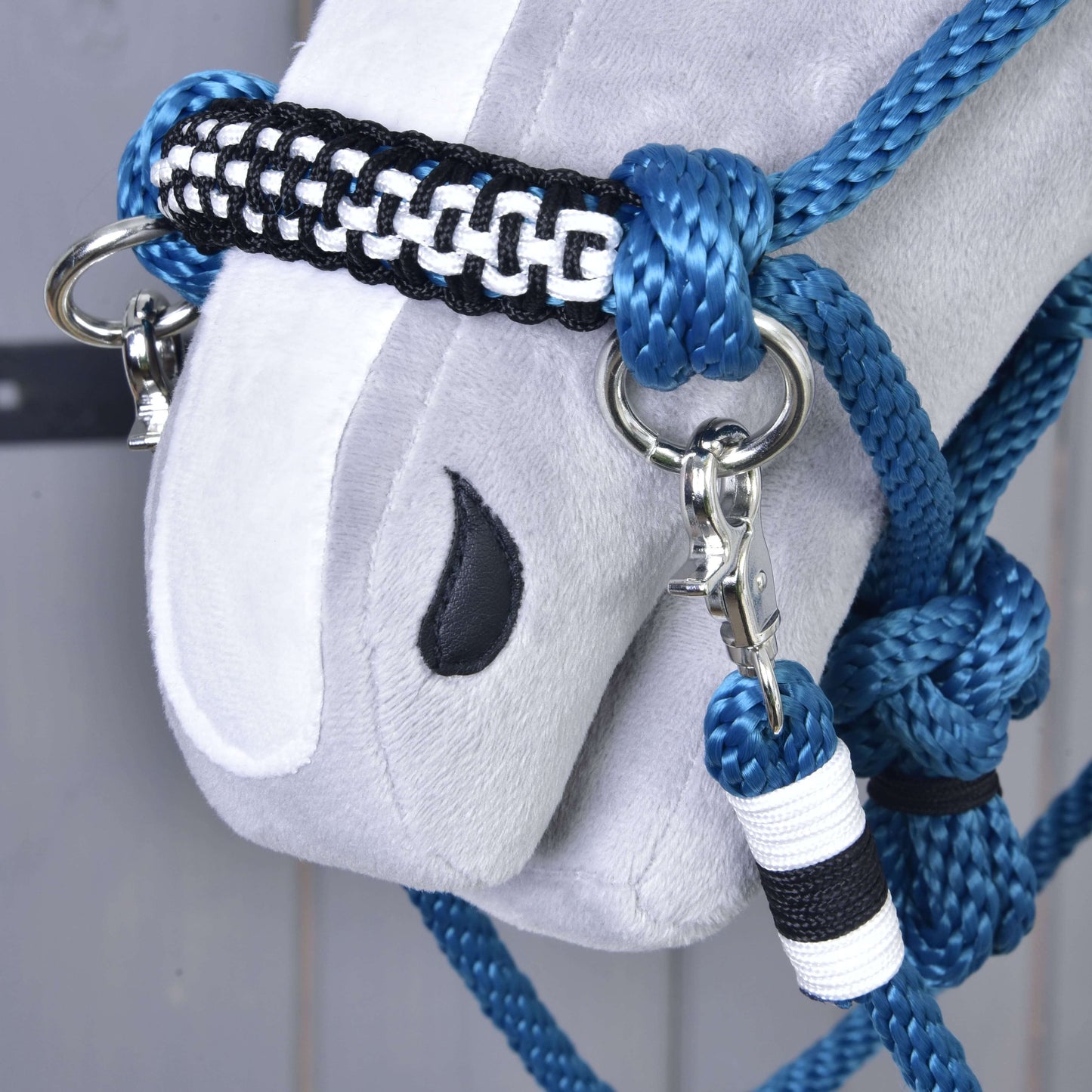 Detail měkké šedé koňské hlavy s vyšitým černým okem, s Hobby Horse LarDen Provazový set Chess – ručně vyráběná modrá, černá a bílá ohlávka s kovovými kroužky a karabinami.