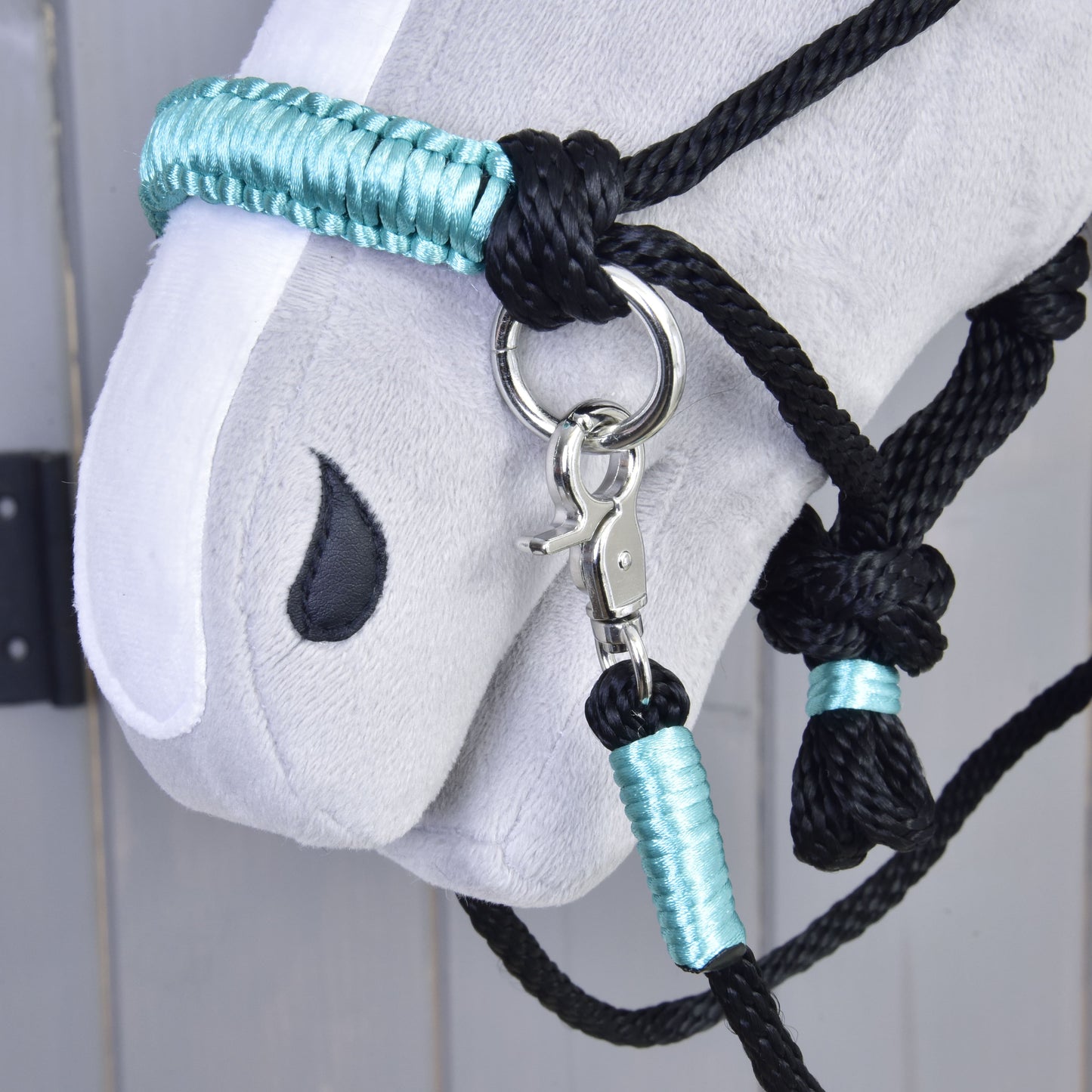 Detail šedé hlavy Hobby Horse s ohlávkou z Provazového setu Turquoise od Hobby Horse LarDen a ladícími otěžemi s kovovým kroužkem a karabinou, na světle šedém dřevěném pozadí.