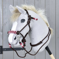 Provazový set York od Hobby Horse LarDen na šedém Hobby Horse s plyšovou hlavou, bílou hřívou a tmavýma očima, s uzdečkou a ohlávkou s červenými a bílými akcenty, před šedým dřevěným pozadím.