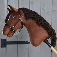 Hobby Horse Rocky s černou ohlávkou od Hobby Horse LarDen, hnědý plyšový kůň na tyči, je zobrazen vedle šedé dřevěné stěny.