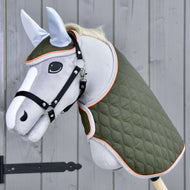 Set Moos od Hobby Horse LarDen s šedým Hobby Horse na dřevěné tyči, černou uzdečkou, zelenou prošívanou dekou a světle modrou čabrakou na šedé dřevěné stěně.