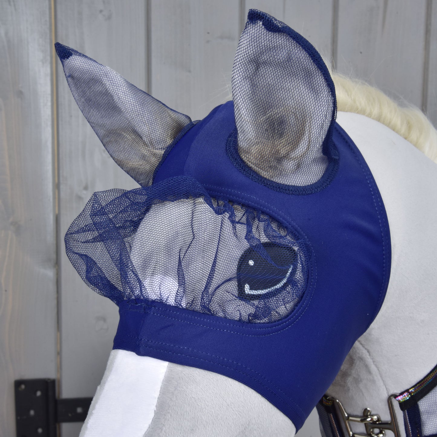 Bílý kůň má na sobě Hobby Horse LarDen Set Fly Combo v námořnické modré se síťovanými kryty uší a očí. Ideální pro styl Hobby Horsing, tato maska chrání oči a uši vašeho koně před hmyzem.