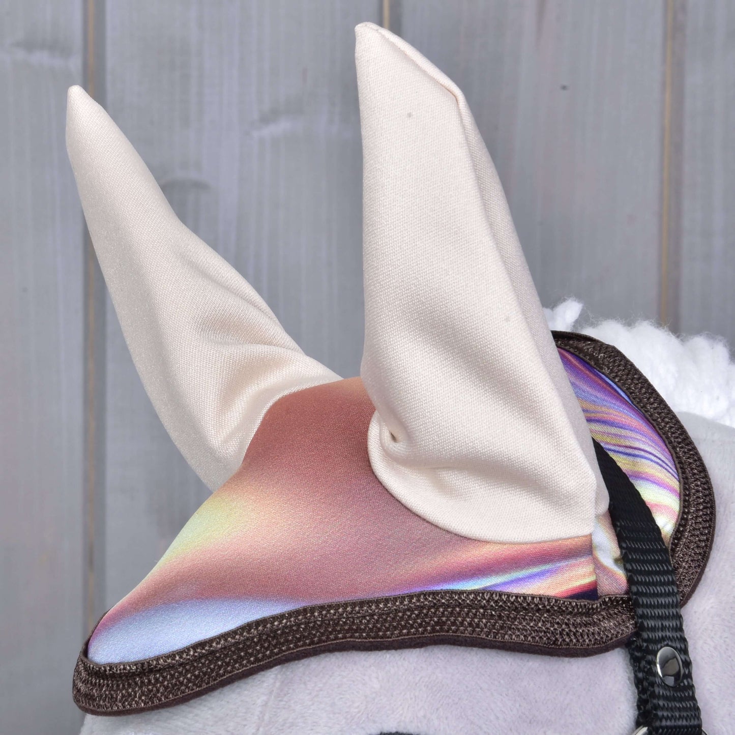 Detail Set Valery od Hobby Horse LarDen – hračka s lesklým, duhovým ušním návlekem a dvěma bílými vzpřímenými látkovými ušima. V pozadí rozmazané dřevěné panely.