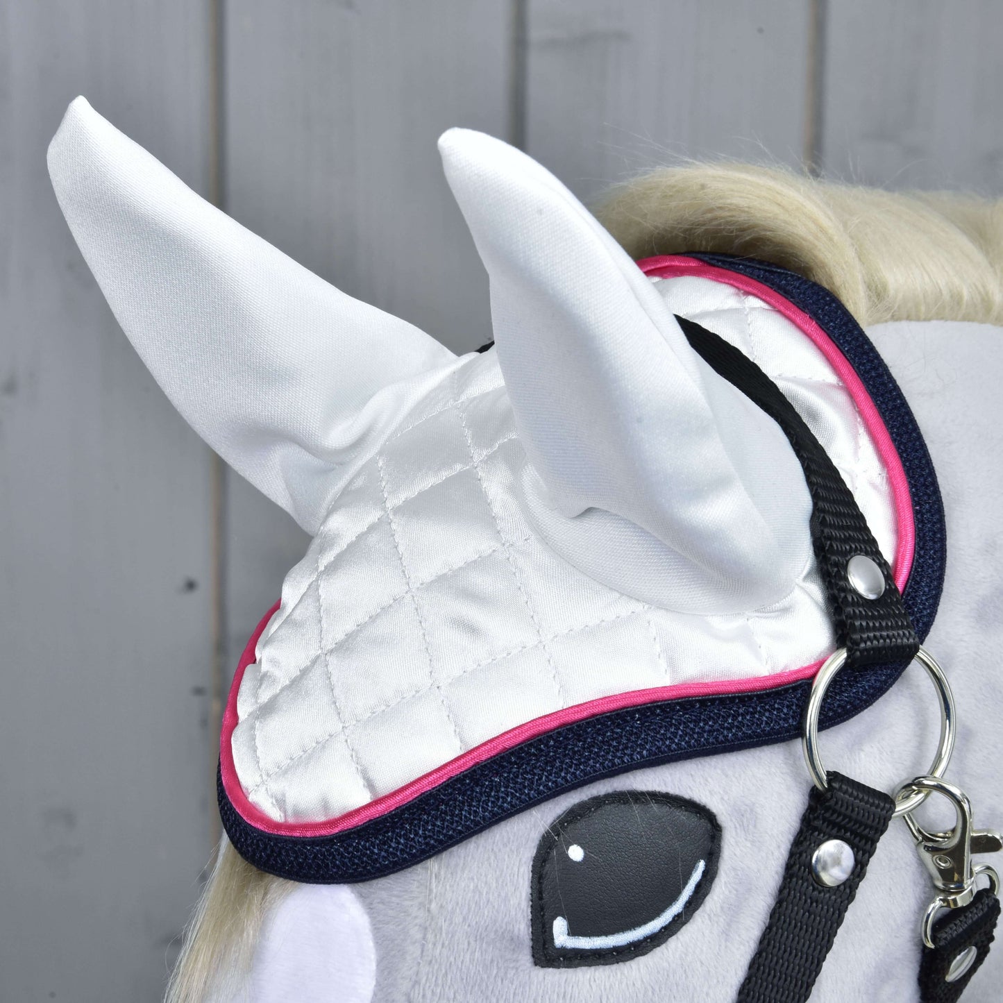 Detail Set Beautiful Star od Hobby Horse LarDen: šedý hračkový kůň s bílou prošívanou čabrakou s růžovým lemem a tmavě modrým okrajem, černými řemínky uzdečky a kreslenýma očima, na pozadí světlého dřevěného obložení — perfektní ochrana koně.