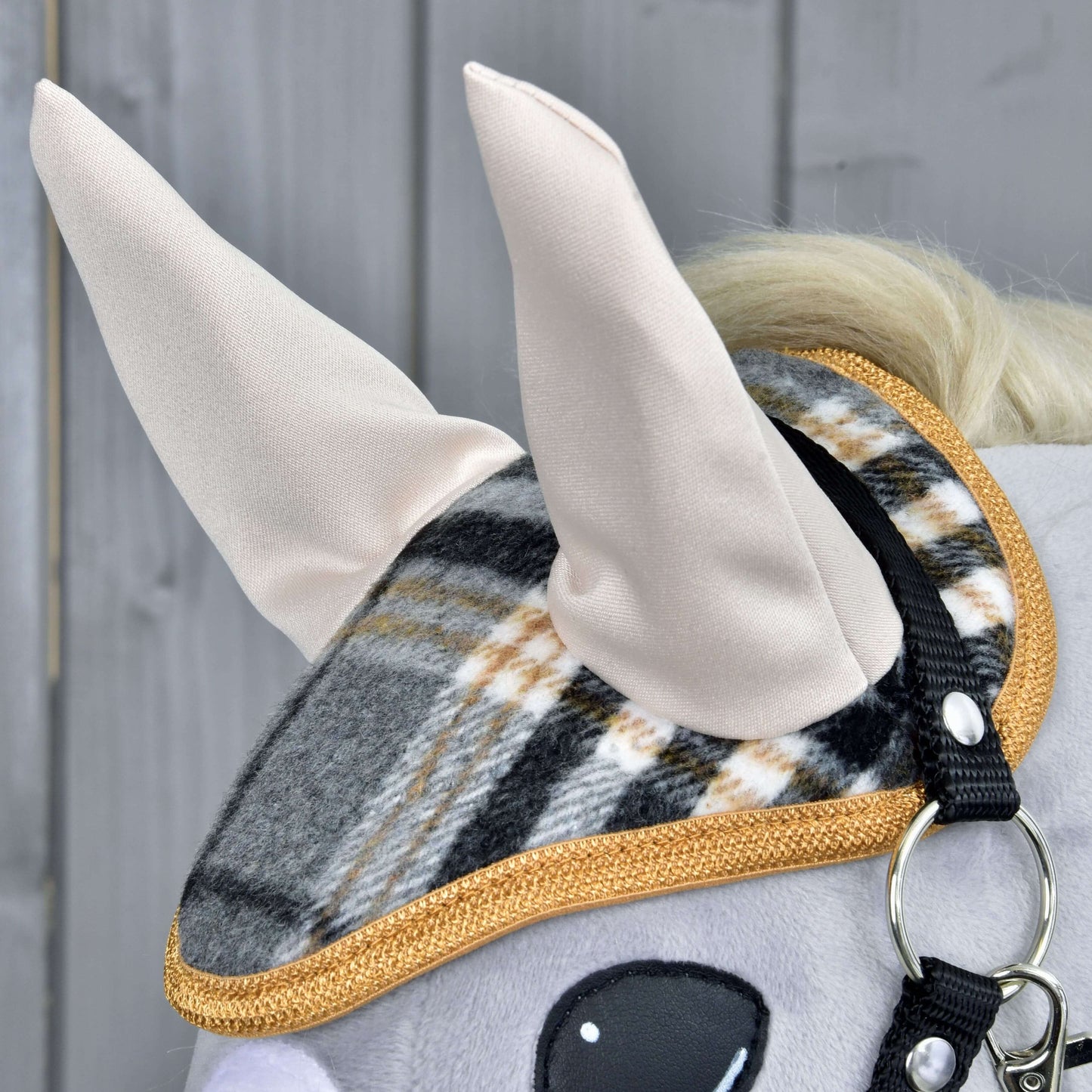 Set England Grey od Hobby Horse LarDen, detail plyšové koňské hlavy s kostkovanou ohlávkou se zlatým lemováním, čabrakou a měkkýma látkovýma ušima na šedém dřevěném pozadí – okouzlující koňská dekorace.