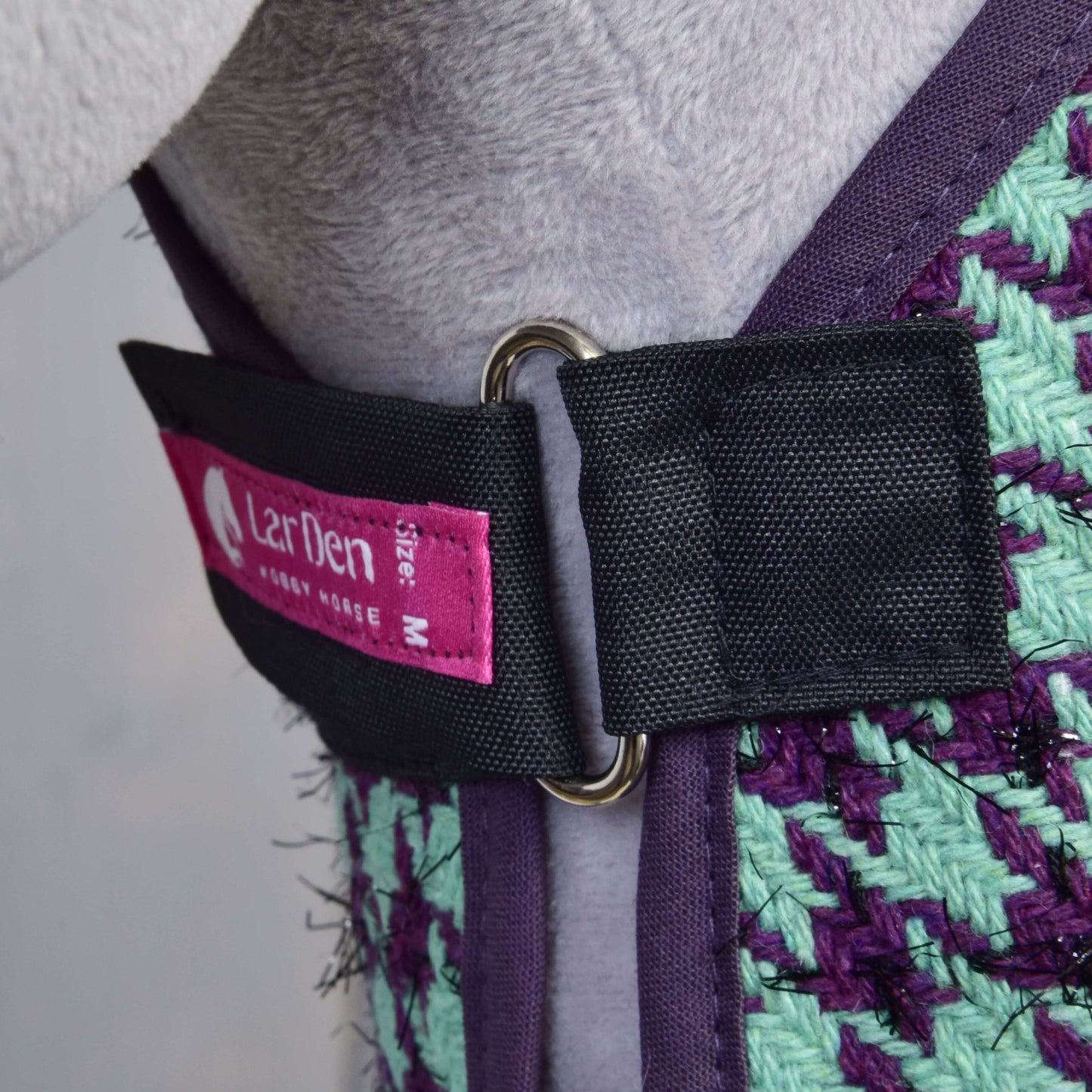 Detail postroje Set Harmony Green od Hobby Horse LarDen v purpurově a zeleně tkaném provedení, s černým řemínkem s kovovým D-kroužkem a růžovým štítkem velikosti M. Nasazeno na světle šedém Hobby Horse.