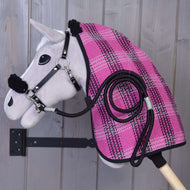Šedý Hobby Horse ze setu „Set Harmony Pink“ od Hobby Horse LarDen je zavěšený na dřevěné stěně a má na sobě růžovo-černou kostkovanou stájovou deku, černou ohlávku a vedle sebe ladící stočené vodítko.