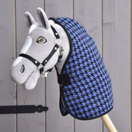 Šedý plyšový hobby horse s černou uzdečkou a dekou Deka stájová Blue od Hobby Horse LarDen s modro-černým vzorem kohoutí stopy, upevněný na dřevěné tyči a umístěný před stěnou z dřevěných prken.