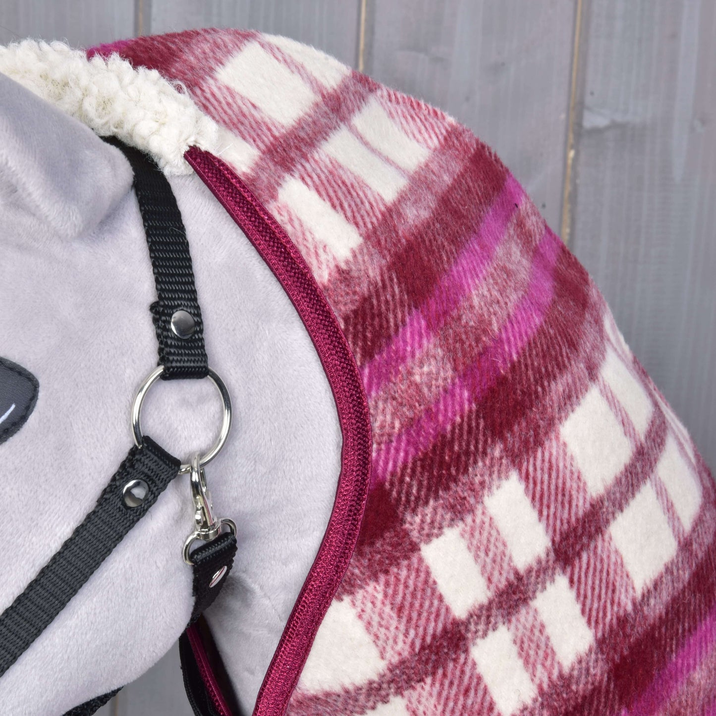 Deka stájová LarDen od Hobby Horse LarDen na šedém koni před dřevěnými prkny, v červeno-růžovo-bílé kostce, s bílou fleecovou podšívkou a ohlávkou.