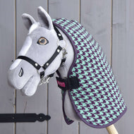 Ručně vyrobený šedý Hobby Horse s černou uzdečkou, oblečený v dece Hobby Horse LarDen „Deka stájová Green“, vystavený před dřevěným pozadím.
