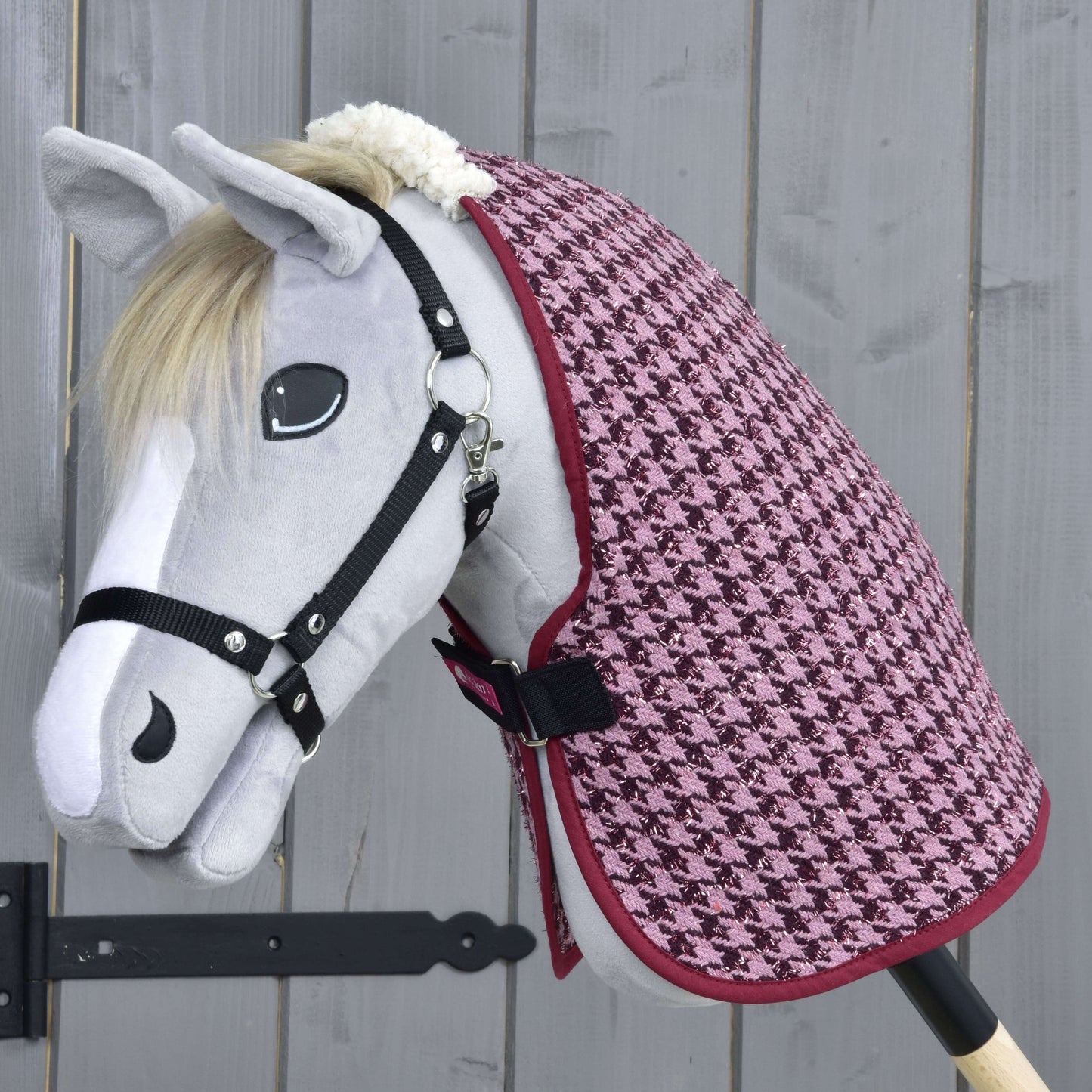 Deka stájová Winter Magic od Hobby Horse LarDen z měkkého PES s růžovým vzorem kohoutí stopy na šedém hobby horse s černou uzdečkou, pózujícím před světle šedým dřevěným pozadím.