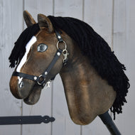 Hobby Horse Sundance s černou ohlávkou od Hobby Horse LarDen s hnědou hlavou inspirovanou rychlostí hřebců, s černou přízovou hřívou, bílou lysinou a černou ohlávkou, upevněný na pevné dřevěné tyči před šedou dřevěnou stěnou.
