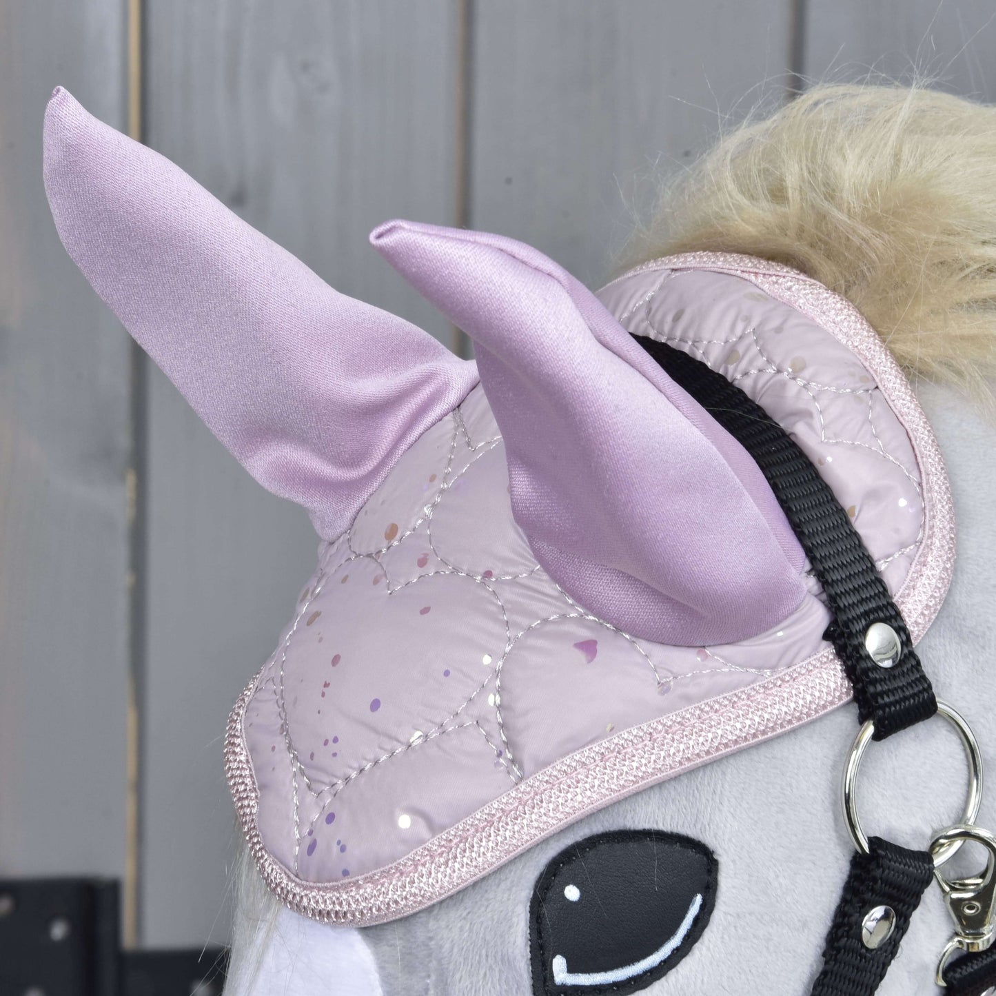 Detail Hobby Horse LarDen Set Sweetest Heart ukazuje jeho světle šedou hlavu, lesklý prošívaný růžový jednorožčí roh, čabraku, černou uzdečku a dřevěné pozadí.