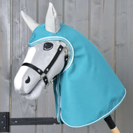 Pláštěnka Turquoise od Hobby Horse LarDen na šedém Hobby Horse s černou uzdečkou a tyrkysovou kapucí ve stylu pláštěnky, s realisticky tvarovanou hlavou s černými a bílými detaily, na světlém dřevěném pozadí.