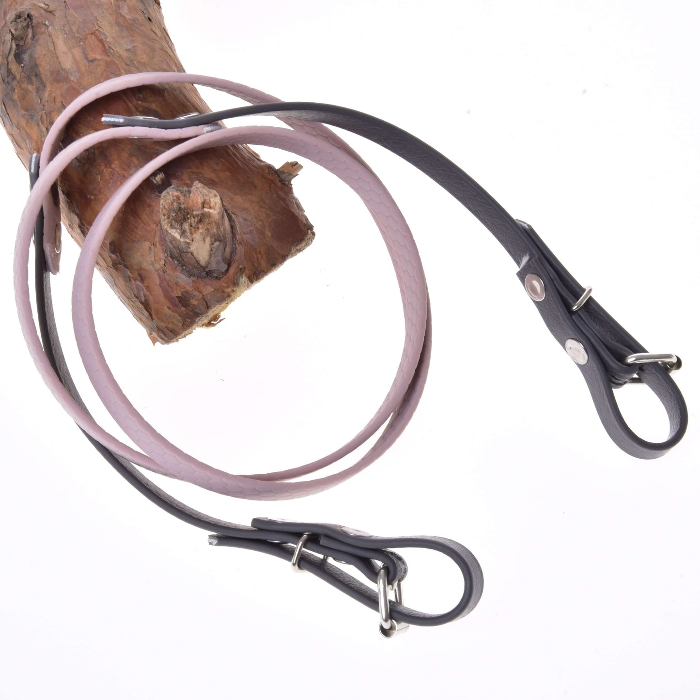 Otěže pogumované Dark Grey/pink od Hobby Horse LarDen dvakrát omotané kolem světle hnědé dřevěné větve, připomínající kožená vodítka pro psy, na bílém pozadí.