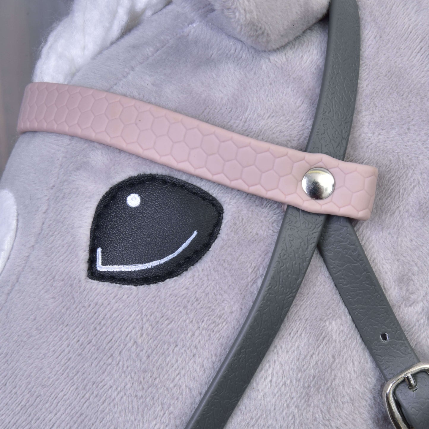 Detail „Kompletní uzdečky šedé s růžovou čelenkou“ od Hobby Horse LarDen na plyšovém koni, zobrazující černě prošité oko a detailní popruhy upevněné kovovým nýtem.