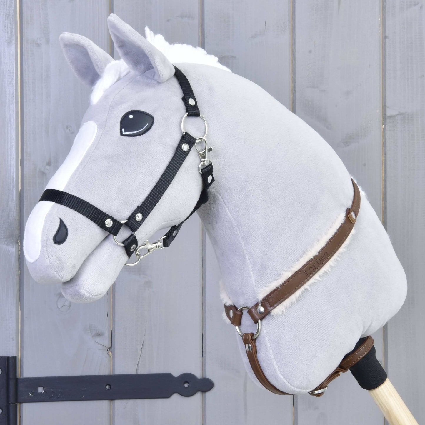 Poprsák s beránkem Walnut od Hobby Horse LarDen na plyšovém šedém Hobby Horse s bílou hřívou, černou uzdečkou, koženými otěžemi a dřevěnou tyčí, na šedém dřevěném pozadí.