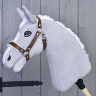 Ohlávka s beránkem z koženky Walnut od Hobby Horse LarDen na šedém plyšovém Hobby Horse s bílou hřívou, hnědou koženkovou uzdečkou a velkýma černýma očima na dřevěné tyči, opřeném o šedou dřevěnou stěnu.