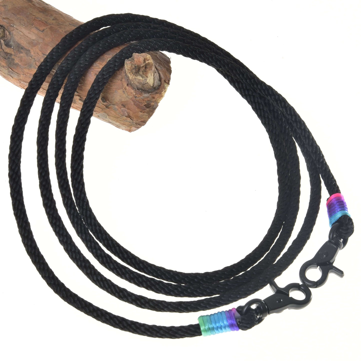 Westernové otěže Montana od Hobby Horse LarDen s černou pletenou šňůrou a karabinami na obou koncích, doplněné modrými, zelenými a růžovými pásky – ideální pro trénink nebo westernové ježdění. Stočené do kruhu na bílém pozadí, se dřevem vlevo nahoře.