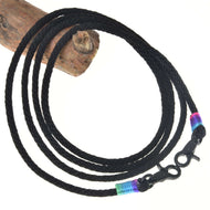 Westernové otěže Montana od Hobby Horse LarDen s černou pletenou šňůrou a karabinami na obou koncích, doplněné modrými, zelenými a růžovými pásky – ideální pro trénink nebo westernové ježdění. Stočené do kruhu na bílém pozadí, se dřevem vlevo nahoře.