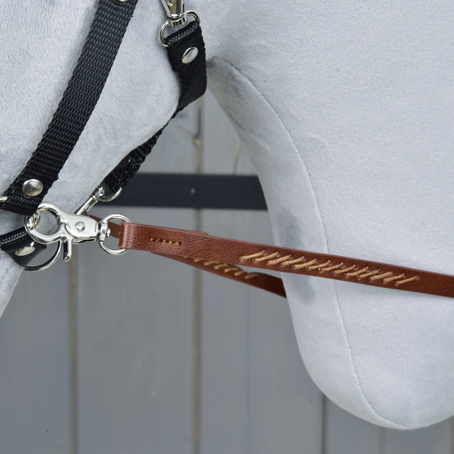 Westernové otěže Dark Brown od Hobby Horse LarDen, detail bílé koňské hlavy v uzdečce s otěžemi připevněnými kovovým klipem, na pozadí světlých dřevěných panelů.