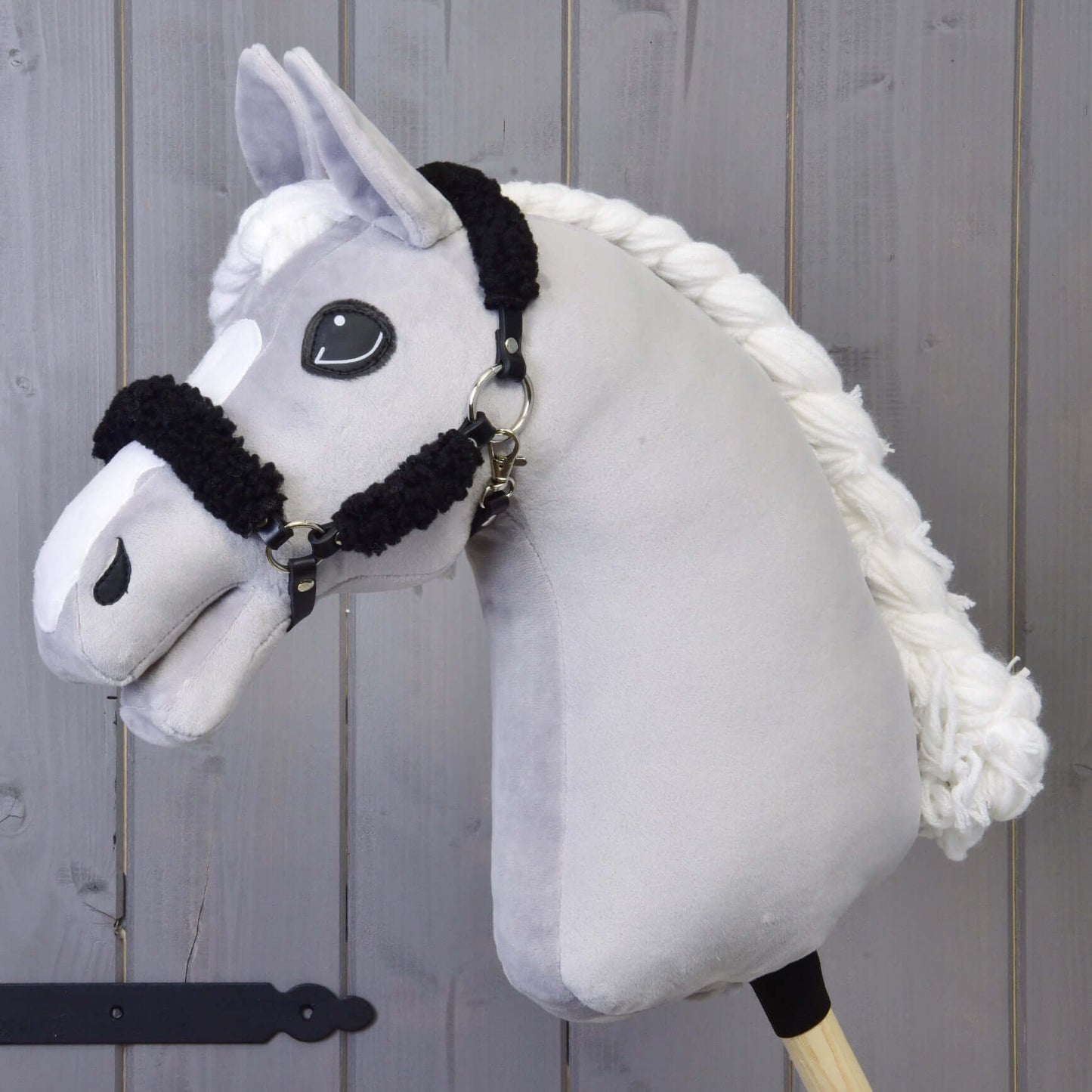 Černá ohlávka z koženky s kompletním černým beránkem od Hobby Horse LarDen na dřevěné tyči, zobrazená před dřevěným obložením.