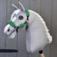 Šedý plyšový Hobby Horse od Hobby Horse LarDen s černou ohlávkou z koženky s kompletním zeleným beránkem před dřevěným panelovým pozadím.