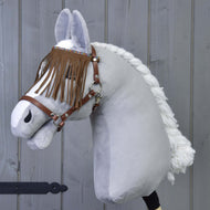 Ohlávka hnědá s třásněmi od Hobby Horse LarDen na plyšovém Hobby Horse se spletenou bílou hřívou, hnědou ohlávkou a třásněmi u očí, zobrazeném před šedou dřevěnou stěnou.