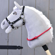 Šedá plyšová hlava Hobby Horse s černou uzdečkou, kovovým udidlem a ručně vyrobeným Nákrčníkem červeným (vel. S) od Hobby Horse LarDen je nasazená na dřevěné tyči na pozadí šedé dřevěné stěny.