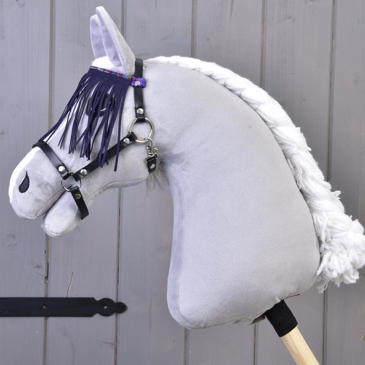 Detail hračky Hobby Horse LarDen se šedým tělem, bílou přízovou hřívou a černou ohlávkou s lila třásněmi, na dřevěném pozadí.
