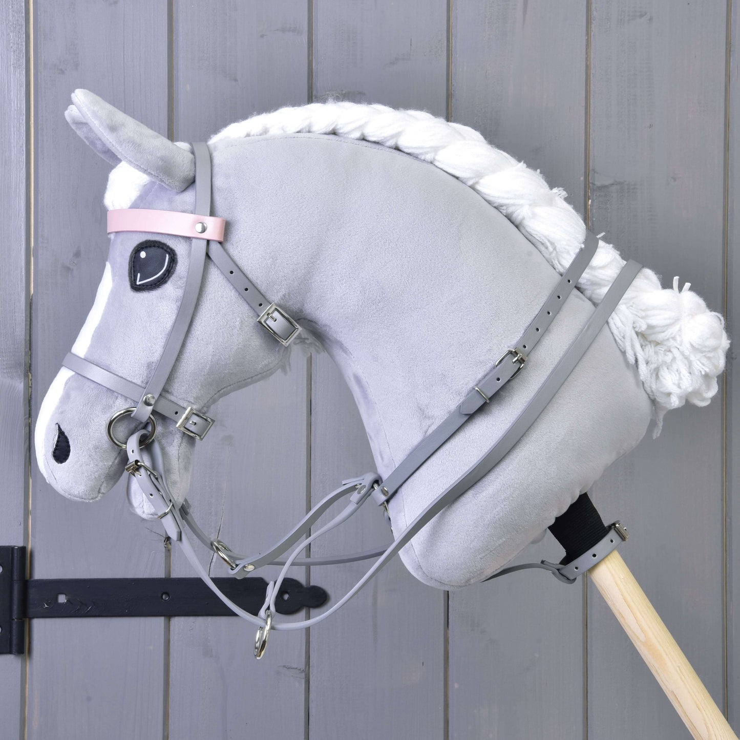 Šedý koženkový set - uzdečka, otěže a martingale od Hobby Horse LarDen na šedém plyšovém koni s bílou hřívou, nasazeném na dřevěné tyči před šedou dřevěnou stěnou.