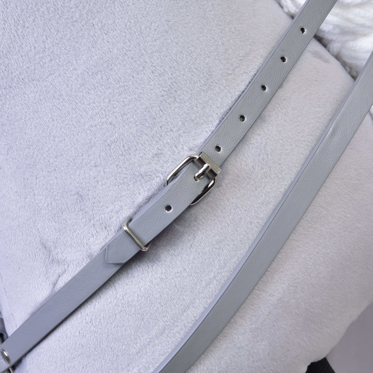 Detailní záběr na Šedý koženkový set - uzdečka, otěže a martingale od Hobby Horse LarDen, zobrazující světle šedý řemínek s kovovou přezkou na světle šedé látce, ideální pro doplnění výbavy vašeho Hobby Horse.